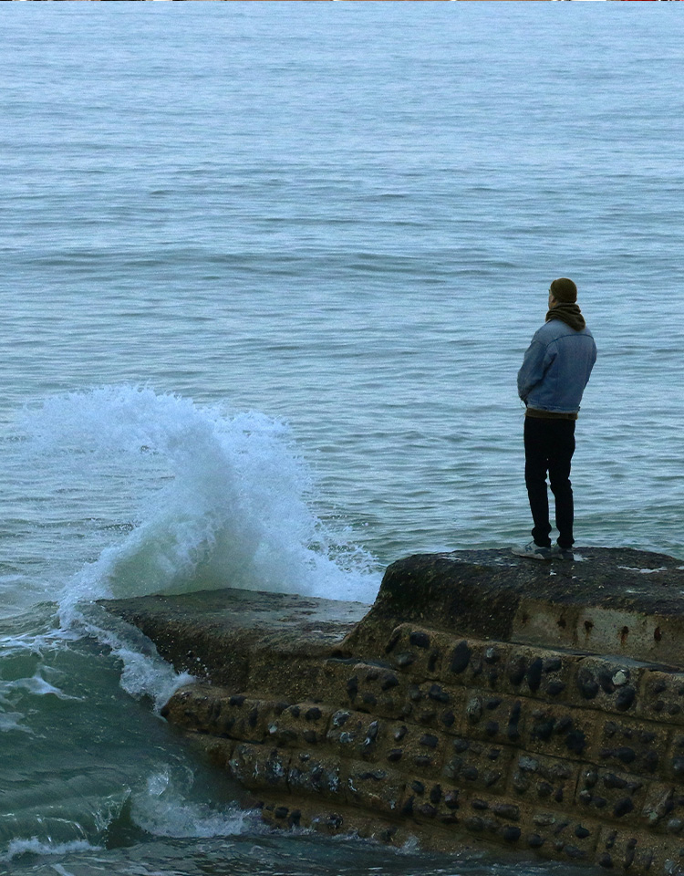 Person standing on a rock by the ocean staring out at the water