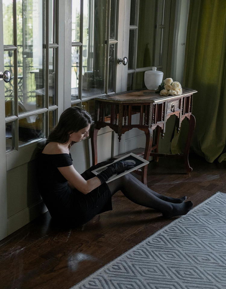 Woman sitting on the floor looking solemnly at a portrait of someone who has passed