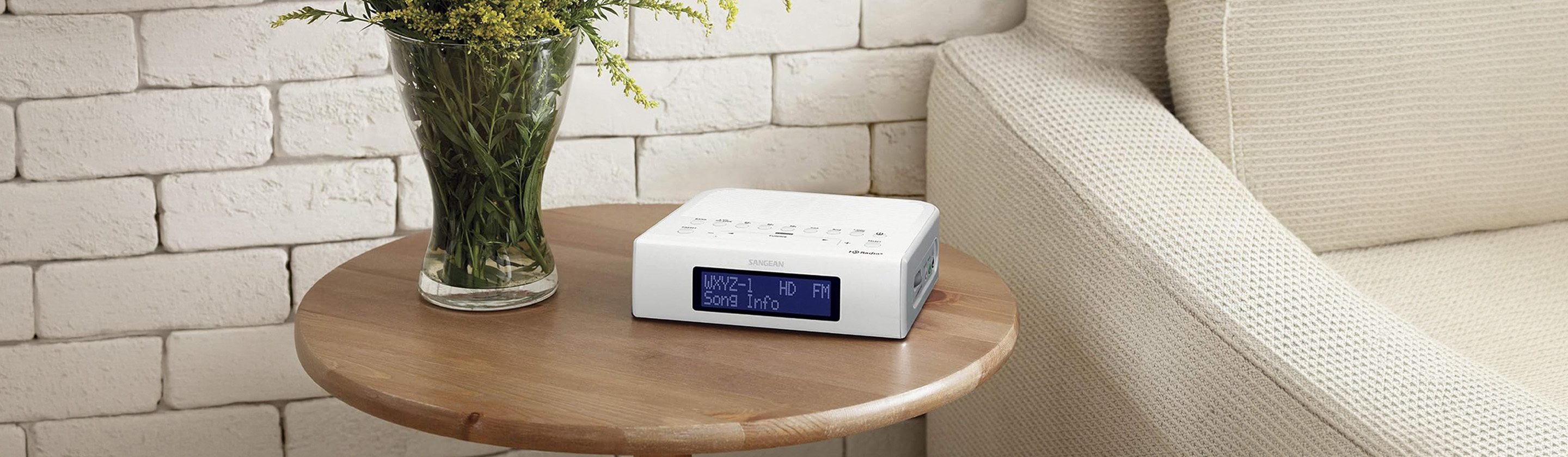Image of white HD radio device sitting on a small end table next to a vase of flowers and a light coloured couch