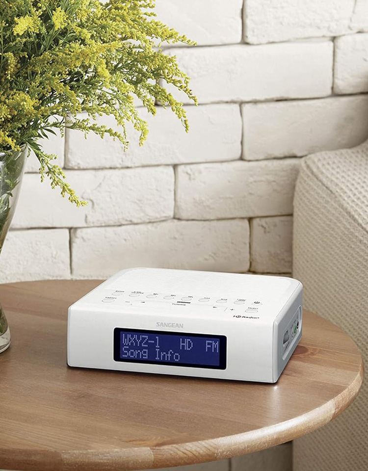 Image of white HD radio device sitting on a small end table next to a vase of flowers and a light coloured couch