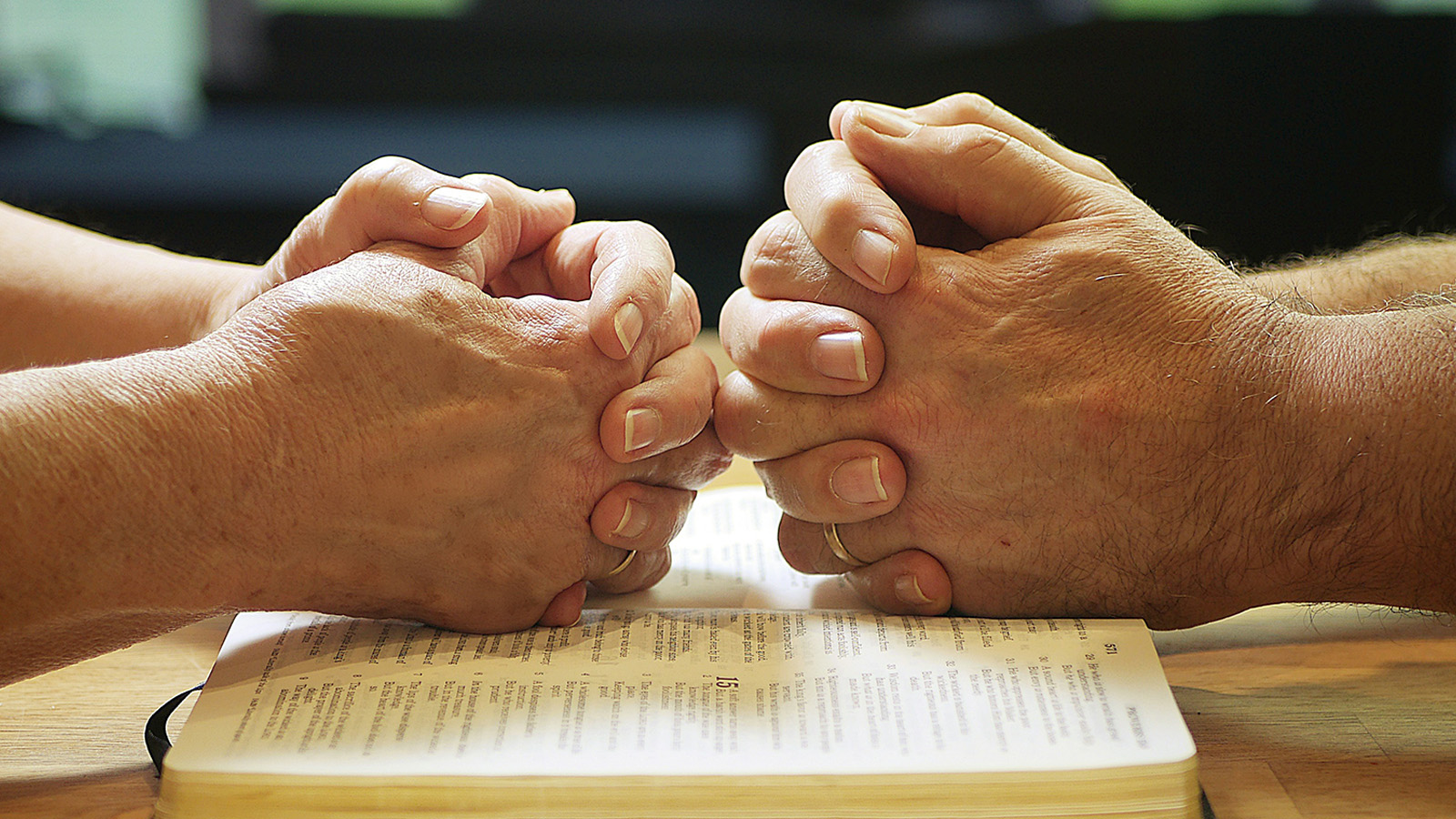 Image of two sets of hands praying over a bible