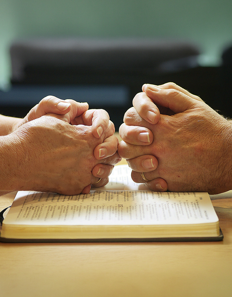 Image of two sets of hands praying over a bible
